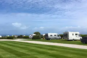 Wohnmobile und Campingbusse auf einem gepflegten Campingplatz, mit Rasen, Kiesweg und Bäumen im Hintergrund.