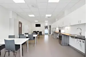 Gemeinschaftsküche im Campinghaus mit Küchenzeile, Spüle, Geschirrkorb und Tischen mit Stühlen.