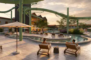 Rund um den Pool stehen Liegestühle und Sonnenschirme, im Hintergrund Gebäude und ein überdachter Bereich mit Bögen.