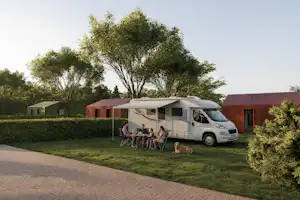 Wohnmobil mit Vorzelt auf dem Campingplatz, davor Sitzgruppe und Kinderstühle, im Hintergrund Hecken und Bäume.