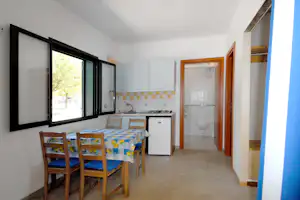 Essbereich in einer Ferienwohnung: Tisch mit Stühlen, Küchenzeile mit Herd und Kühlschrank, große Fenster, Flur mit Türen.