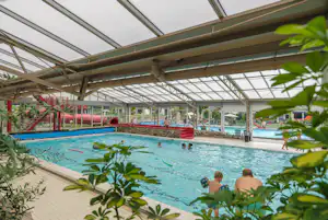 Innenpool mit roter Rutsche, Überdachung aus Glas und Stahlträgern, Kinder planschen im Wasser.
