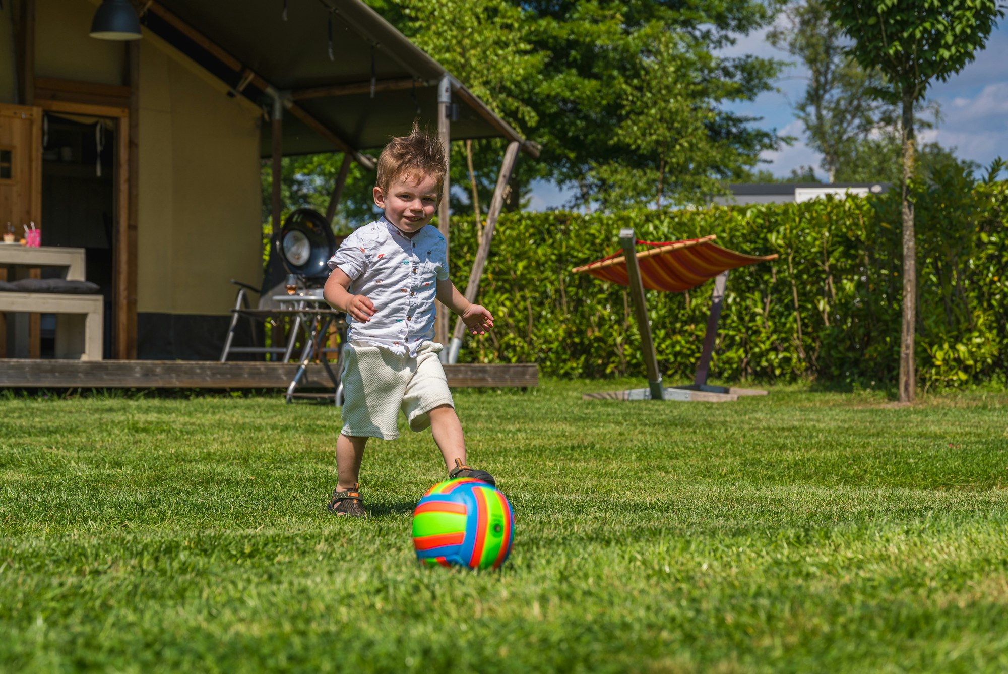 Ardoer Vakantiepark Ackersate - Kind spielt mit einem Ball auf der Wiese vor einem Glamping-Zelt