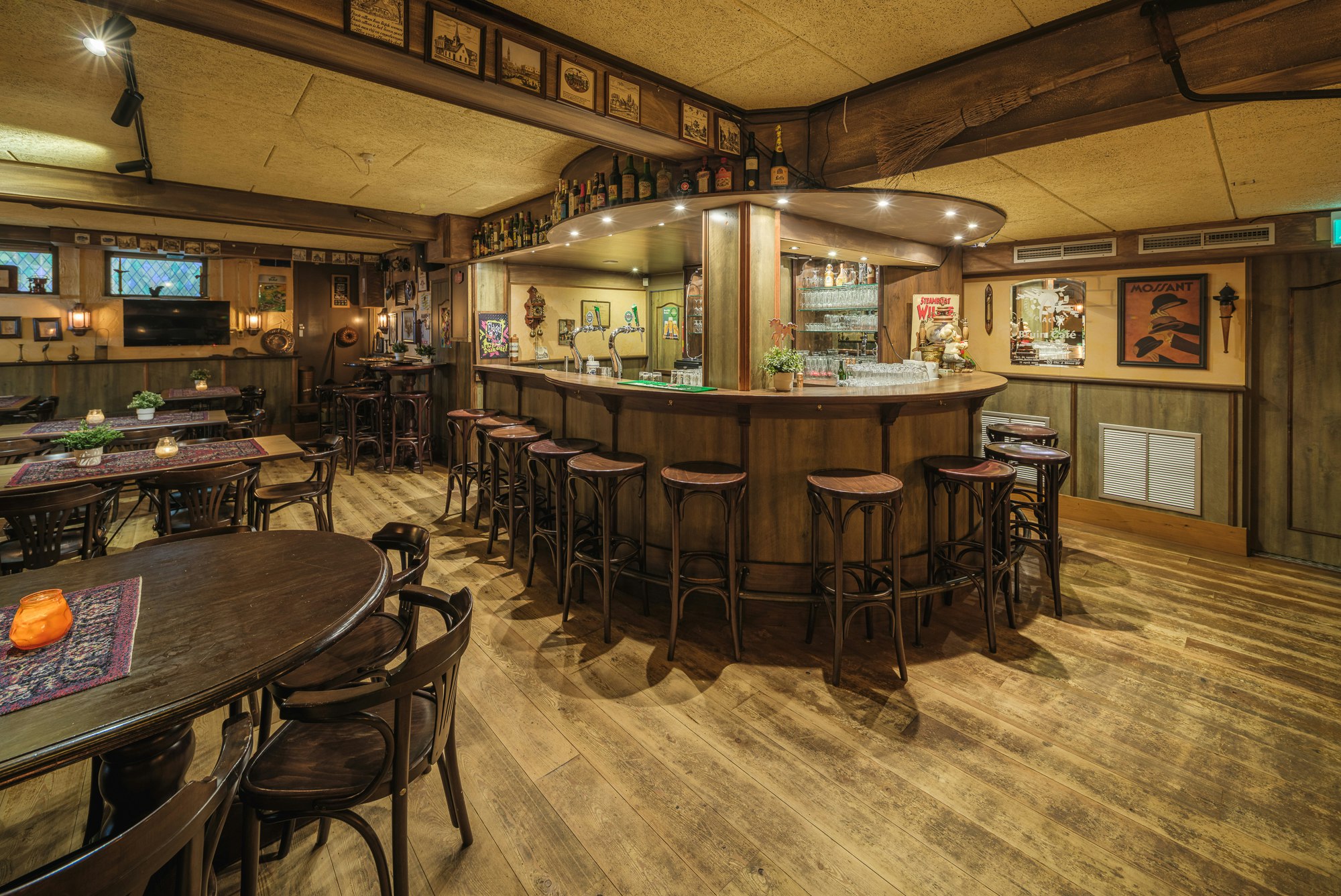 Barbereich im Campinghaus mit Holztheke, Getränkeflaschen, Barhockern und Tischen im Innenraum.
