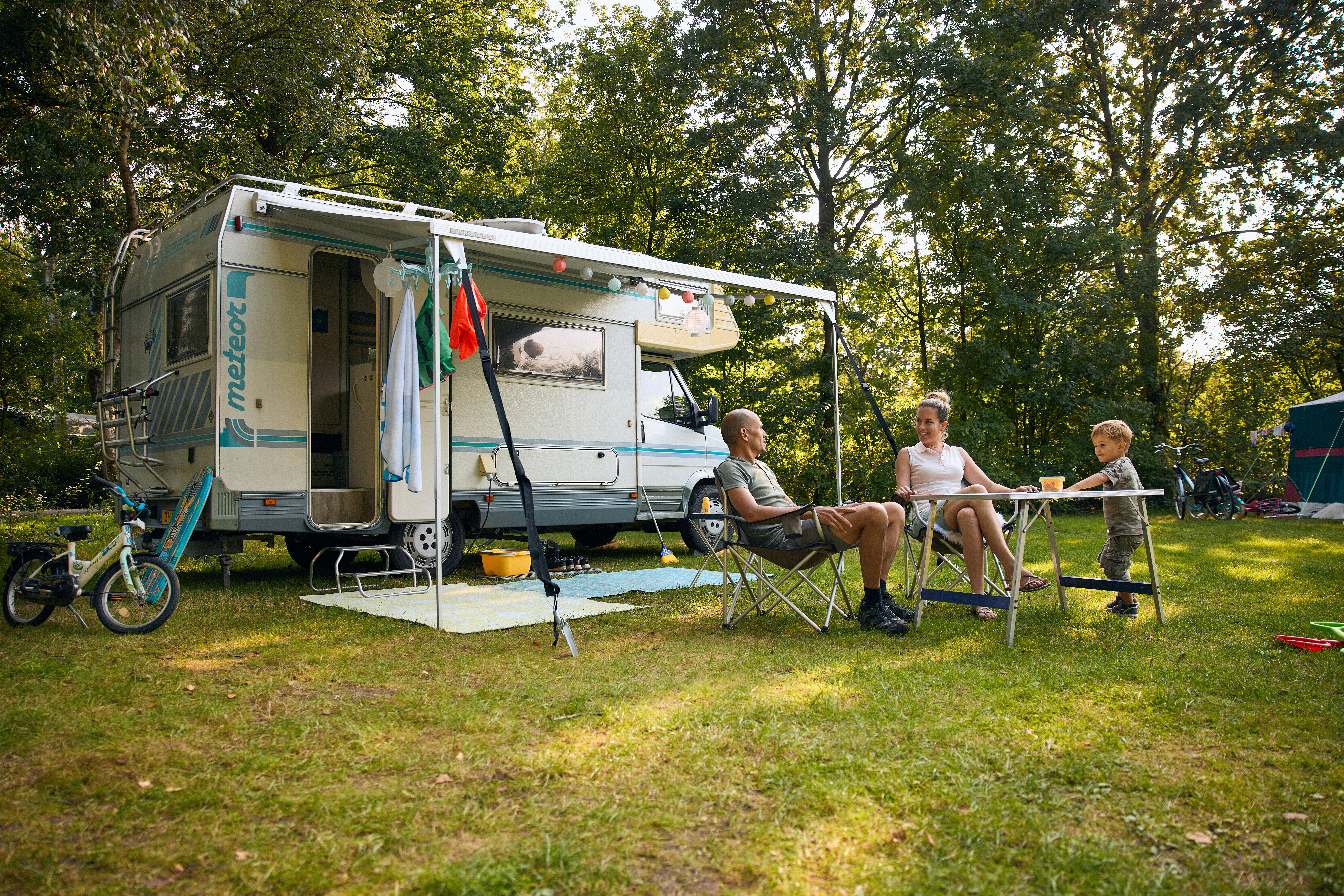 Vakantiepark Beekse Bergen - Familie auf Standplatz im Halbschatten auf einer Wiese von Bäumen umgeben