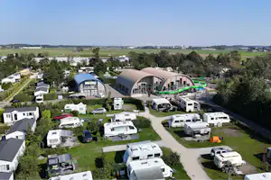 Luftaufnahme eines Campingplatzes mit Wohnmobilen und Wohnwagen, gepflegten Stellplätzen, Wegen und einem großen Gemeinschaftsgebäude mit Glasfront.