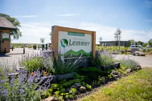Schild „Lemmer“ am Camping-Eingang mit Blumenbeeten, Wegen und Wohnwagen-Stellplätzen im Hintergrund.