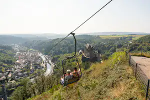 Seilbahn mit Sitzbank und Blick ins Tal: Fluss, Waldhügel und eine Burganlage im Vordergrund.