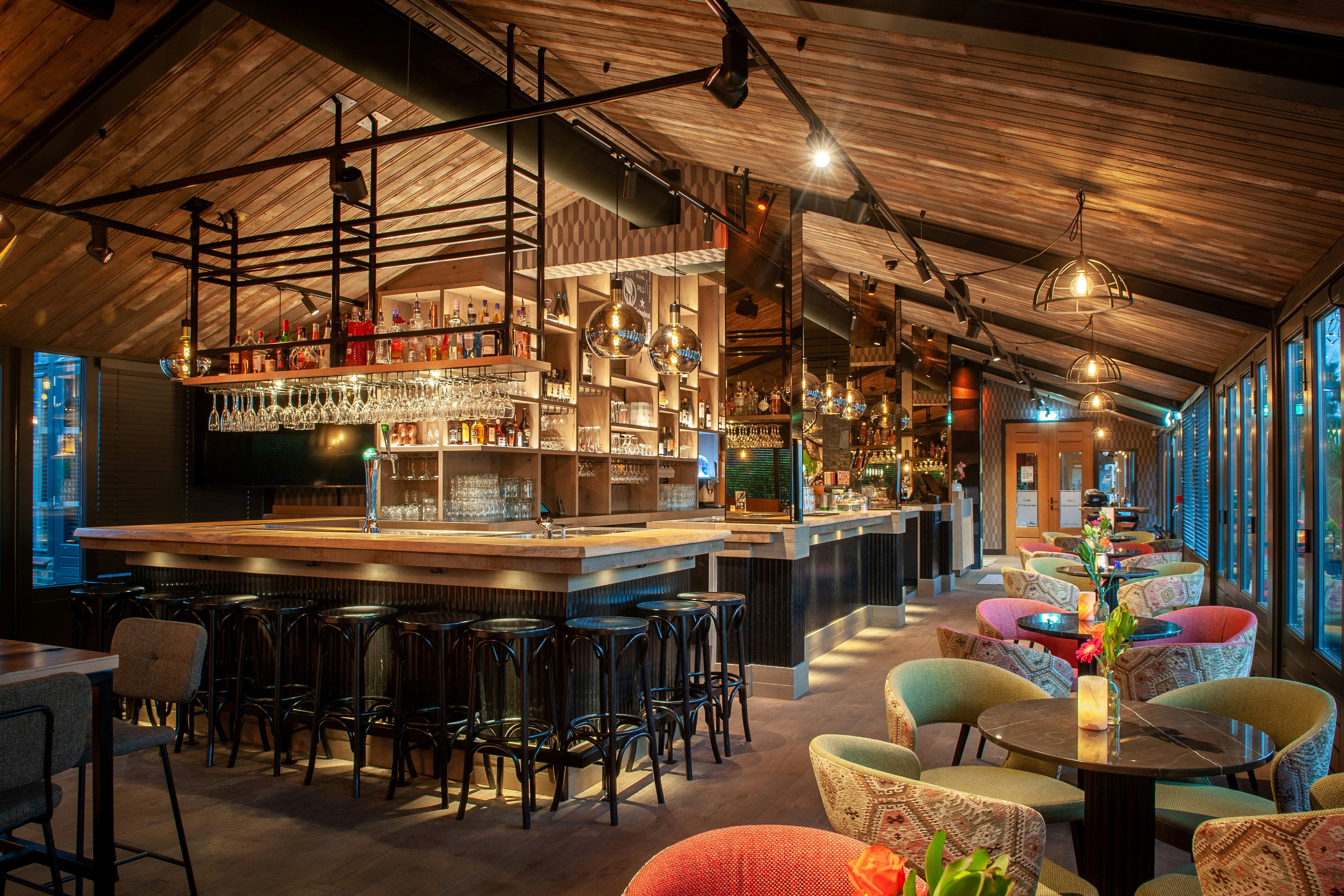 Campingbar mit Holzdecke, beleuchtetem Tresen, vielen Flaschen im Regal und Sitzgelegenheiten im Innenbereich.