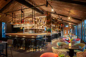 Campingbar mit Holzdecke, beleuchtetem Tresen, vielen Flaschen im Regal und Sitzgelegenheiten im Innenbereich.