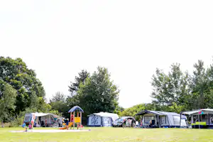 Zelte auf einem grünen Campingplatz, mehrere Wohnzelte mit Markisen und bunten Details, umgeben von Bäumen.