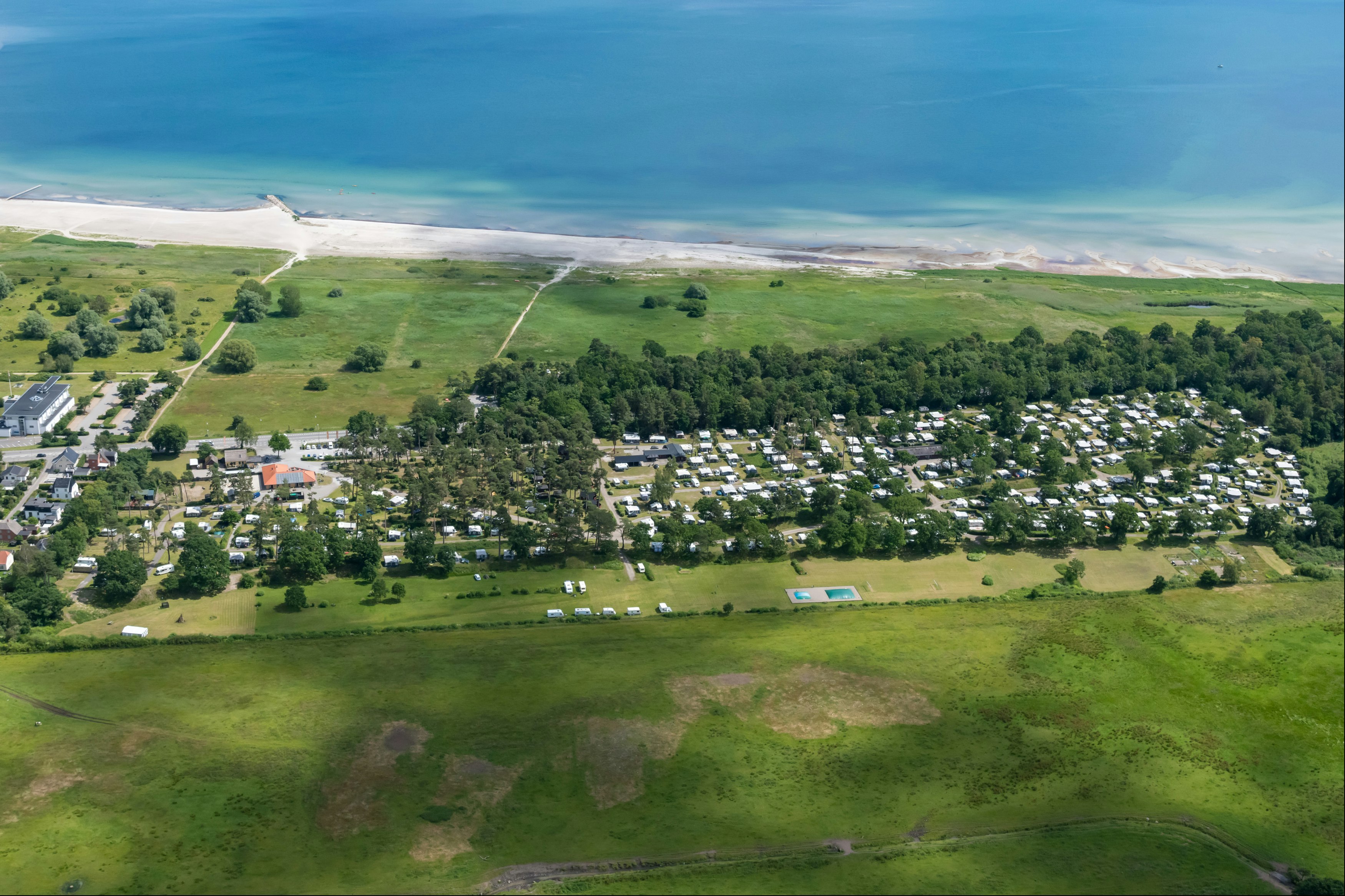 Luftaufnahme eines Campingplatzes an der Küste mit Wohnwagen, Wegen, Grünflächen und Blick auf das Meer.