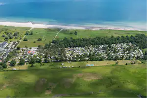 Luftaufnahme eines Campingplatzes an der Küste mit Wohnwagen, Wegen, Grünflächen und Blick auf das Meer.