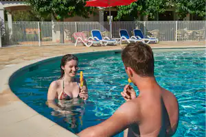 Zwei Personen im Camping-Pool, einer hält ein Schwimmspielzeug, im Hintergrund Liegestühle und Zaun.