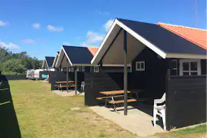 Mehrere Camping-Hütten mit Holzfassade, überdachten Terrassen und Gartenmöbeln stehen am Weg auf einer Rasenfläche.