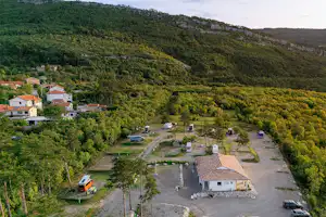 Campingplatz mit Stellplätzen und Wohnmobilen, umgeben von grünen Hügeln und einem kleinen Gebäude im Tal.