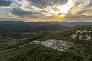 Luftaufnahme eines Campingplatzes im Tal mit Gebäuden, Wegen und umgebenden Hügeln bei Sonnenuntergang.