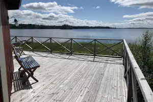 Holzterrasse am See mit Bank und Geländer, Blick auf ruhiges Wasser und gegenüberliegende Uferlinie.