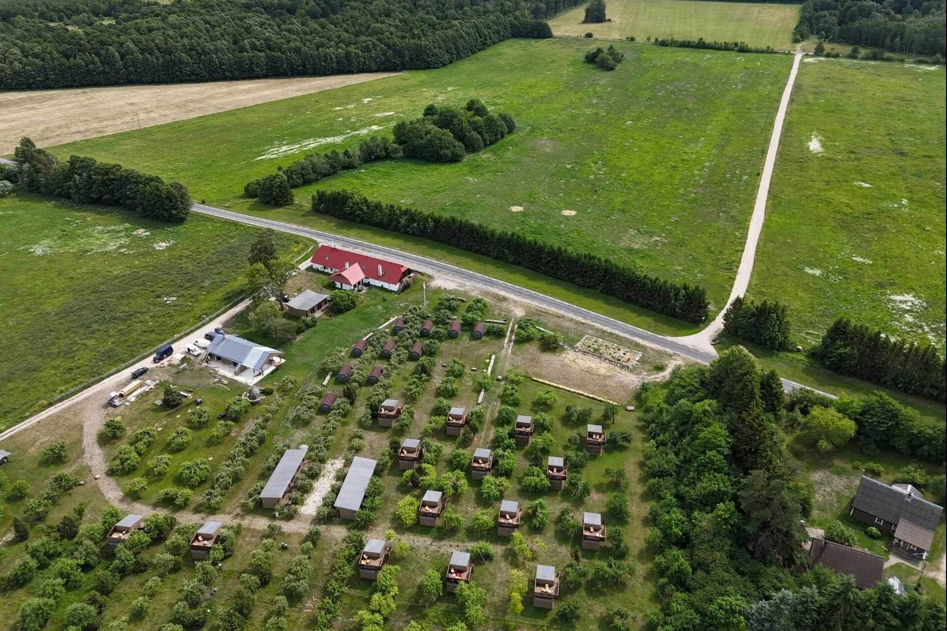 Luftaufnahme eines Campingplatzes mit kleinen Stellplätzen, Wegen und Bäumen, umgeben von grünen Wiesen und einem Fluss im Hintergrund.