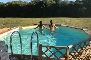 Kinder im Camping-Pool, umgeben von Rasen und Hecken, mit Leiter am Beckenrand und Holzgeländer.