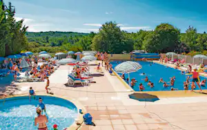 Großer Campingpool mit Kinderbereich, Liegen und Sonnenschirmen, daneben ein zweiter Pool und Wege zwischen Bäumen und Hügeln.