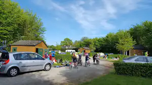 Campingplatz-Weg mit geparkten Autos, Zelten und Wohnwagen, umgeben von Bäumen und kleinen Gebäuden.