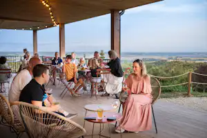 Familie beim Essen auf der Camping-Terrasse, Holzstühle und Tische, Lichterkette und weite Aussicht ins Tal.