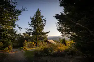Zelt auf einem Campingplatz am Waldrand, mit Kiesweg, Bäumen und Blick in die Ferne.