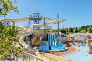 Wasserrutschen und mehrere Pools auf dem Campingplatz, mit Sonnenschirmen, Liegen und Zäunen aus Holz und Metall.