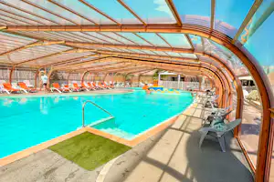 Überdachter Poolbereich mit türkisfarbenem Schwimmbecken, Liegestühlen und Sonnenschirmen unter Holzbogen-Gewölbe.