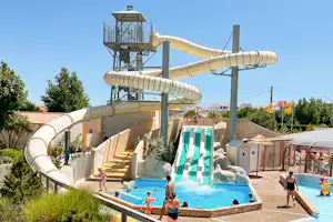 Wasserrutschen über einem Pool auf dem Campingplatz, mit Sonnenschirmen, Liegen und Bäumen im Hintergrund.