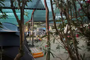 Zelte auf einem Campingplatz zwischen Bäumen, mit Tisch und Stühlen am Weg, im Hintergrund ein weiteres Zelt.