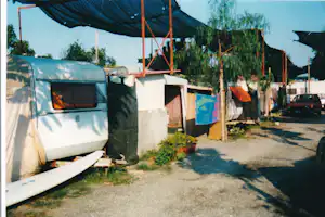 Wohnmobil auf einem Campingplatz-Stellplatz, daneben Zelte und Wäsche, Sichtschutz und Bäume entlang des Weges.