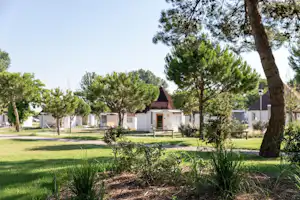 Reihe weißer Ferienhäuser auf einem Campingplatz, umgeben von Rasen, Bäumen und einem gepflegten Gartenweg.