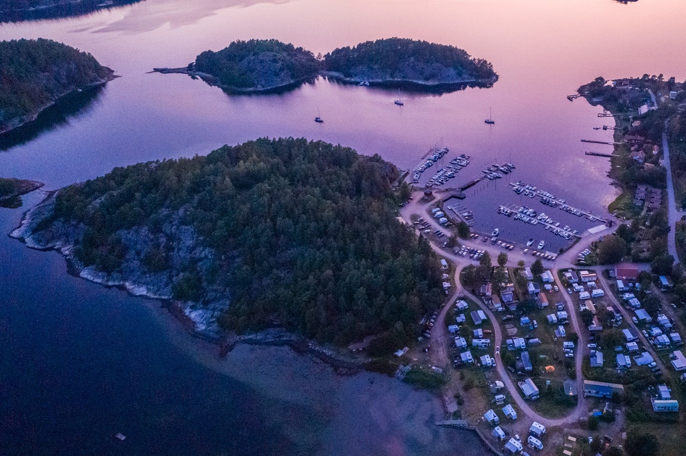 Luftaufnahme eines Campingplatzes am See mit Bootsstegen, Stellplätzen und Wegen zwischen bewaldeten Inseln.