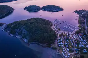 Luftaufnahme eines Campingplatzes am See mit Bootsstegen, Stellplätzen und Wegen zwischen bewaldeten Inseln.