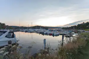 Bootshafen am Campingplatz mit vielen Segelbooten, Stegen und Wasser bei Sonnenuntergang, im Hintergrund Ufer und Bäume.