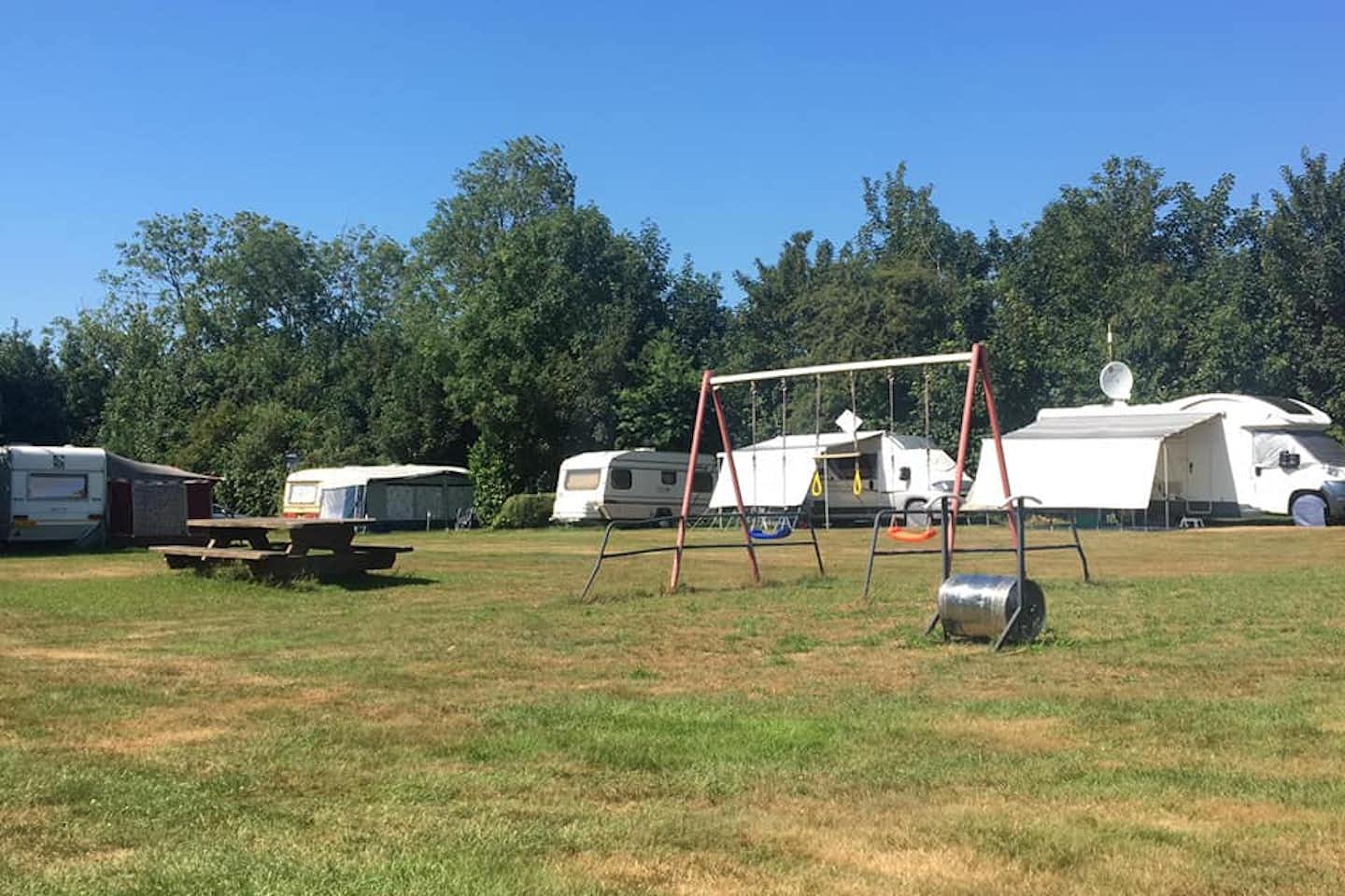 Vodatent @ Camping Eefting - Blick auf weitläufige Wiese mit Schaukel und Picknicktisch, dahinter Standplätze mit Wohnwagen