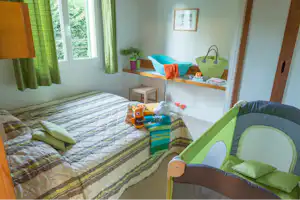 Schlafbereich im Wohnwagen mit Doppelbett, Kinderbett, bunten Kissen und Fensterblick ins Grüne.