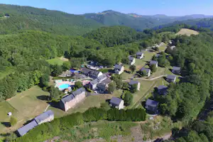 Luftaufnahme einer Campinganlage mit Pool, mehreren Gebäuden und Wegen inmitten grüner Hügel und Bäume.