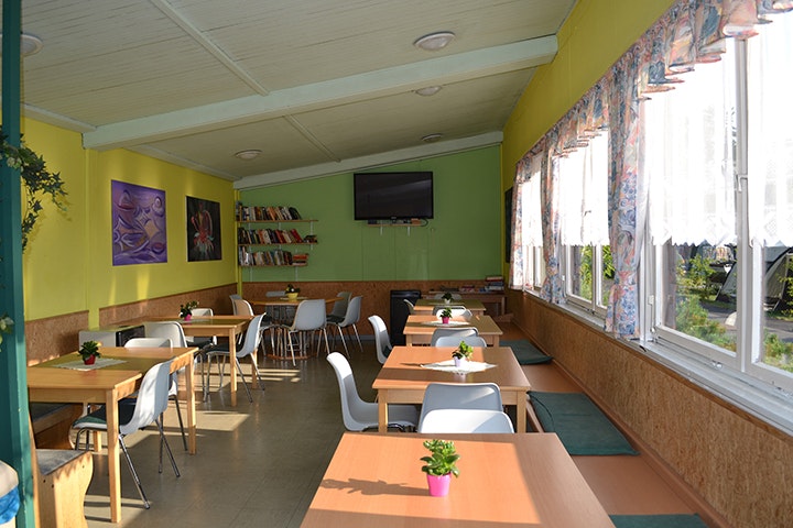 Waldcamping - Aufenthaltsraum mit Tischen und Stühlen, Fernseher an der Wand