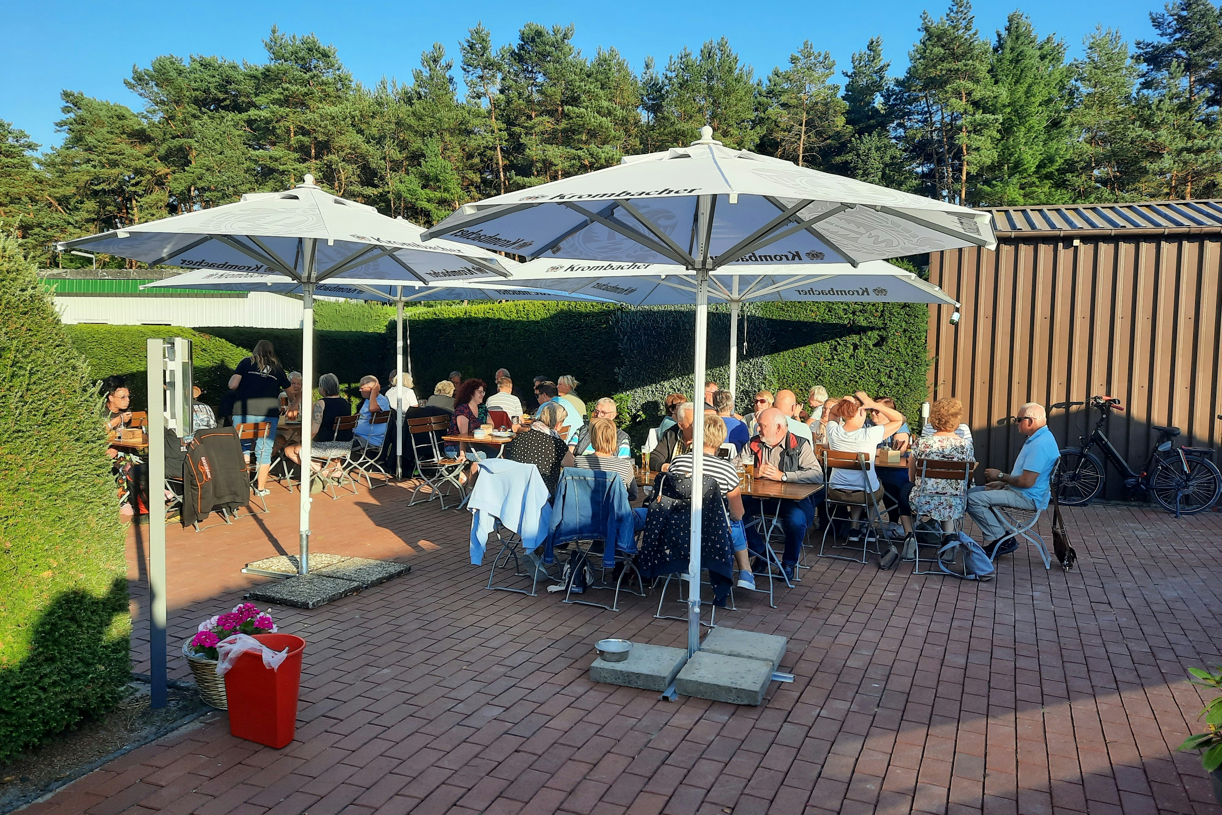 Waldesruh Camping CMA  Watercamp Waldesruh - Biergarten mit Gästen, die unter Sonnenschirmen sitzen, umgeben von grünen Hecken 