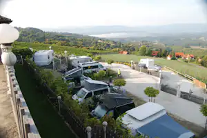 Wohnwagen und Campingbusse auf Stellplätzen am Hang, Blick ins grüne Tal mit Feldern und Häusern in der Ferne.