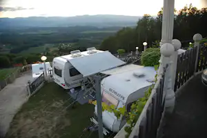 Wohnmobile auf einem Campingplatz mit Blick ins Tal, neben einem Zaun und Sitzgelegenheiten auf der Terrasse.