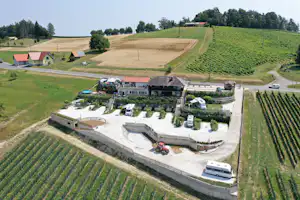 Luftaufnahme einer Campinganlage mit Stellplätzen, Wohnwagen und Pool inmitten von Feldern und grünen Hügeln.
