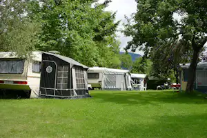 Wohnwagen mit Vorzelt und Markise auf einem grünen Campingplatz, umgeben von Bäumen und weiteren Zelten.