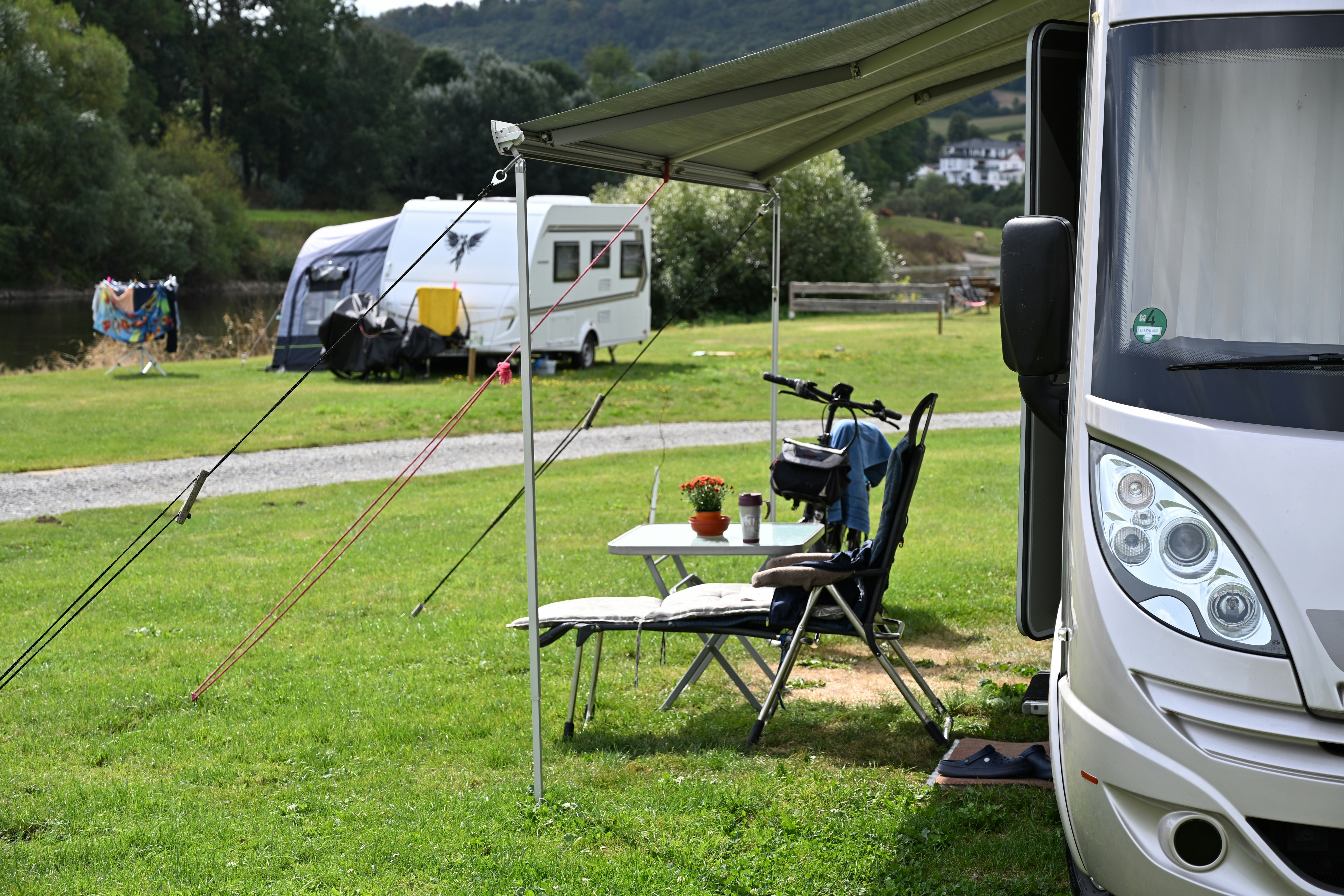 Wohnmobil am Campingplatz mit Vorzelt, Tisch und Campingstühlen auf dem Rasen, im Hintergrund Zelt und Bäume.