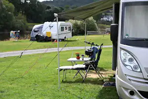 Wohnmobil am Campingplatz mit Vorzelt, Tisch und Campingstühlen auf dem Rasen, im Hintergrund Zelt und Bäume.