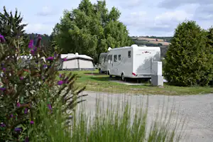 Wohnmobil auf einem Campingplatz neben einem kleinen Zelt, umgeben von Gras, Büschen und Bäumen am Weg.