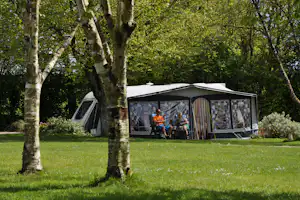 Wohnwagen und Zelt mit Vorzelt auf einem grünen Campingplatz, umgeben von Bäumen und Rasen.